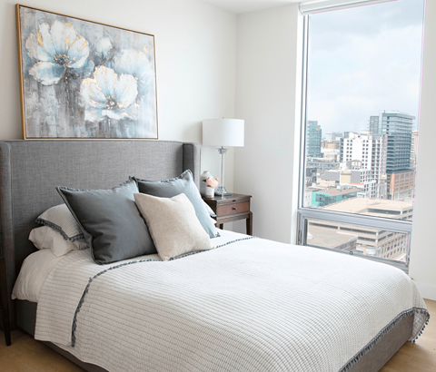 A bedroom with a large bed and a city view through the window.