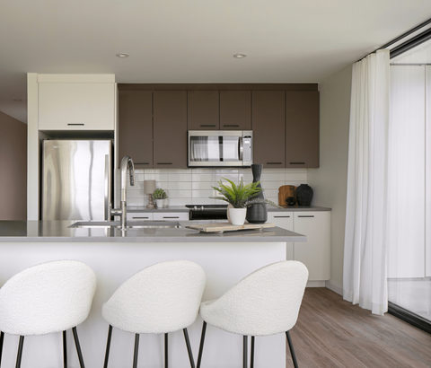 A modern kitchen with white chairs and brown cabinets.