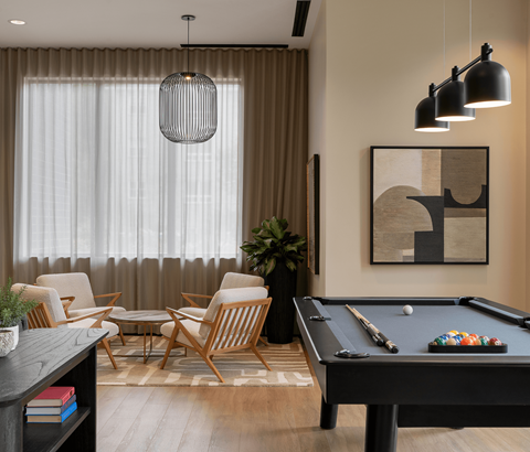 A pool table is in the middle of a room with a chair and a plant.