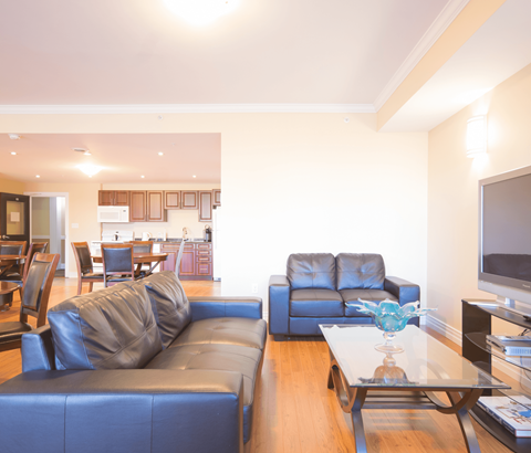A living room with a black leather couch and a glass coffee table.
