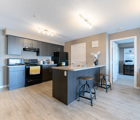 A kitchen with a black refrigerator and wooden floors.
