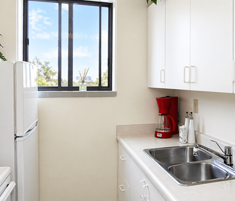 A kitchen with a white fridge, white cabinets, and a window.