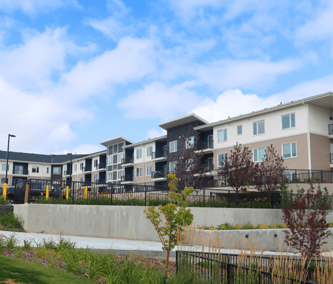 A row of modern townhouses with a concrete wall and greenery in the foreground.