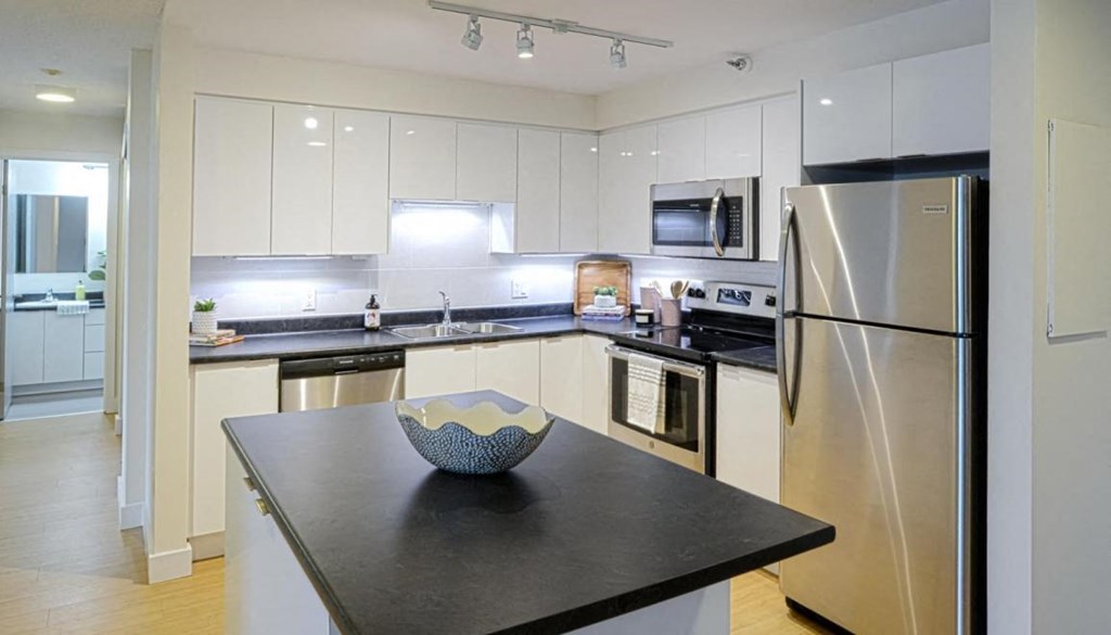 A modern kitchen with a black countertop and stainless steel appliances.
