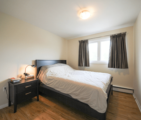 A bedroom with a bed, nightstand, and window.