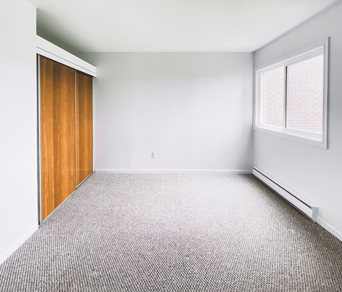 A room with a carpeted floor and a window with blinds.