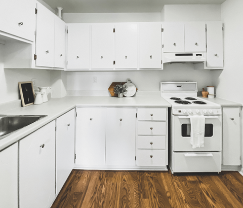 A white kitchen with wooden floors and a stove top oven.
