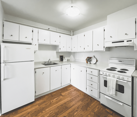 A white kitchen with wood floors and white appliances.