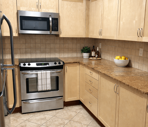 A kitchen with a stainless steel oven and microwave above a counter with a bowl of lemons on it.