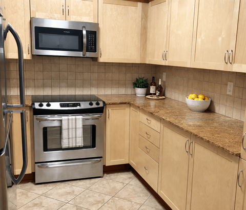 A kitchen with a stainless steel oven and microwave above a counter with a bowl of lemons on it.