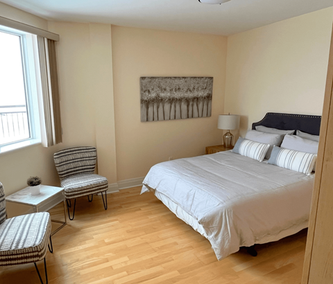 A bedroom with a bed, chair, and painting on the wall.
