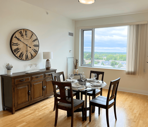 A dining room with a table set for four and a large clock on the wall.