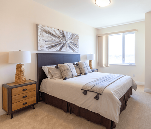 A bedroom with a large bed, a nightstand with a lamp, and a painting on the wall.
