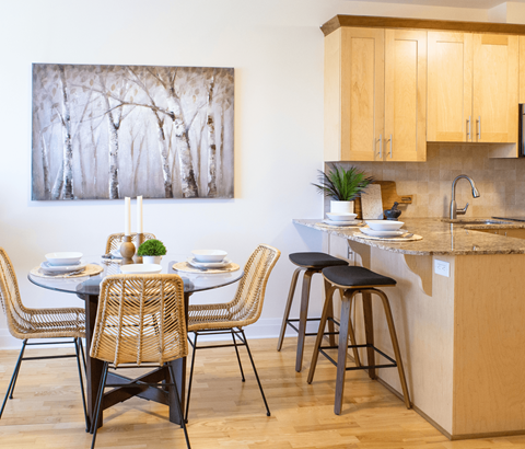 A kitchen with a table set for two and a painting of trees on the wall.