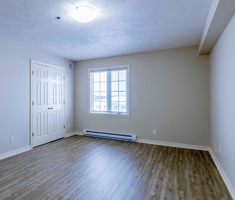 A room with a white door, a window, and a wooden floor.