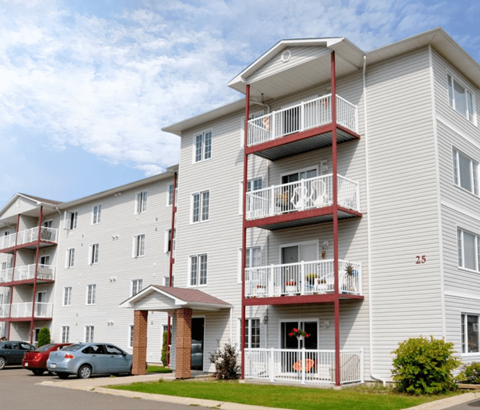 A white apartment building with red balconies and a car parked in front.