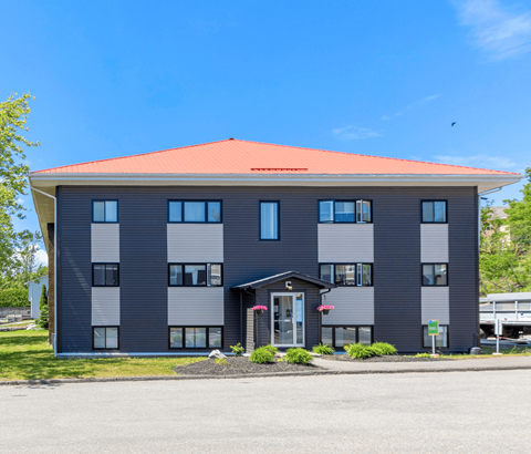A grey building with a red roof and a white door.