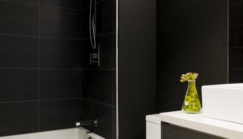 a black bathroom with a white toilet and a vase with a flower