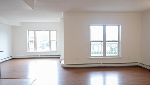 an empty living room with wood floors and two windows