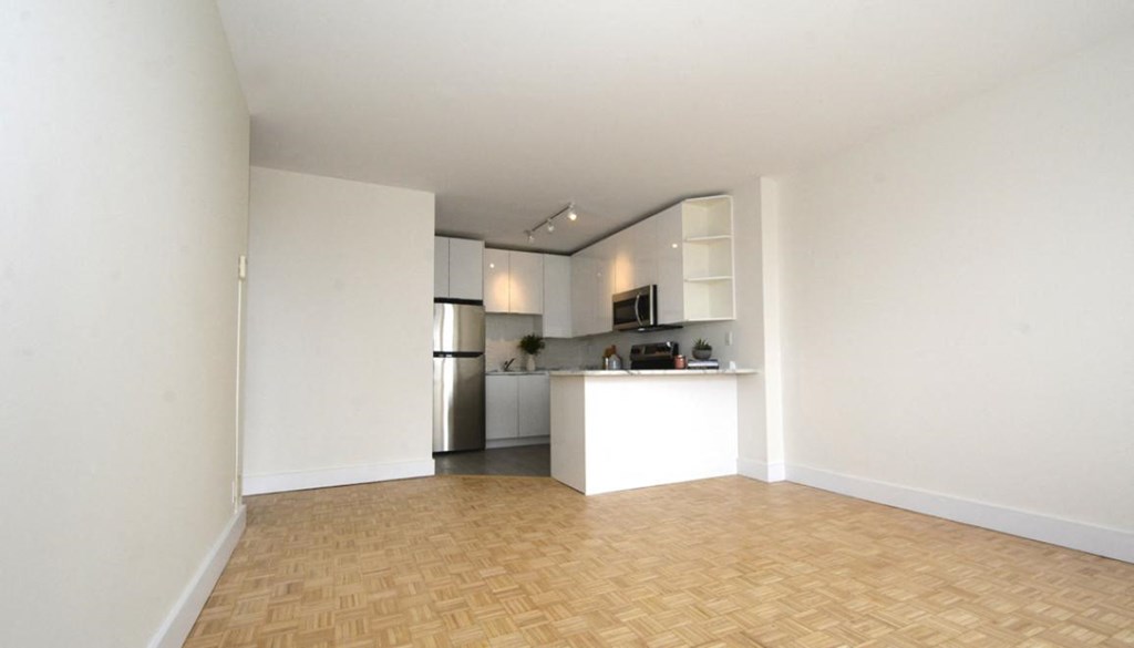 an empty living room with a kitchen in the background