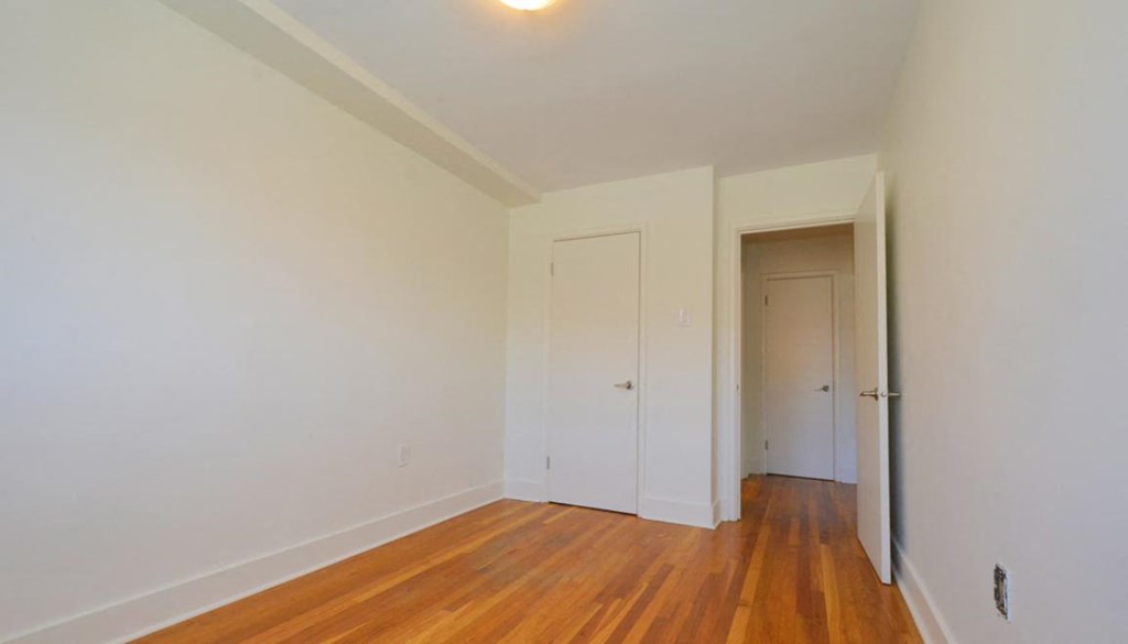 a bedroom with white walls and wood floors and a closet