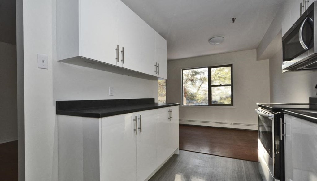 an empty kitchen with white cabinets and a window