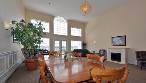 A large wooden dining table surrounded by chairs in a room with a fireplace and a potted plant.