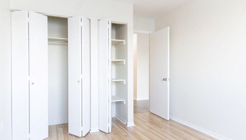 A room with white walls and a wooden floor with four white shelves and a door.