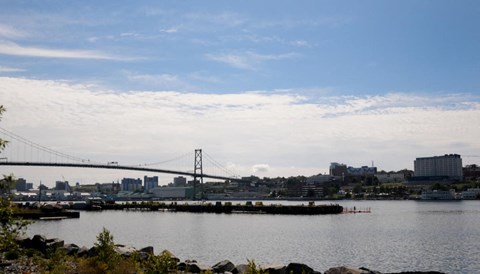 A bridge spans across a calm body of water with a city skyline in the background.