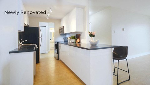 A newly renovated kitchen with black and white appliances and a wooden floor.