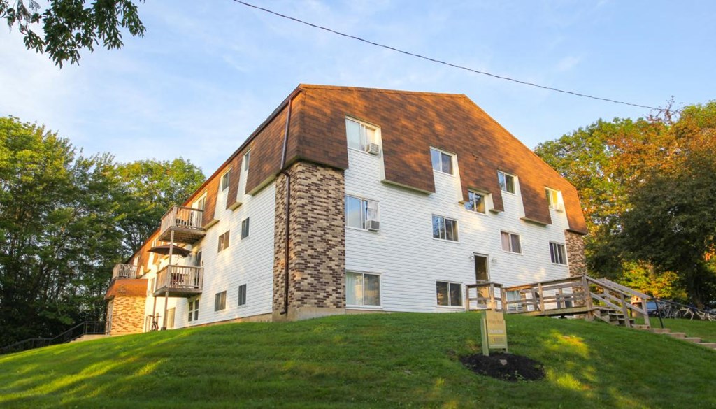 A white building with a brown roof and a stone chimney.