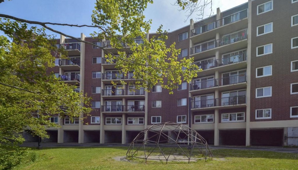 A playground with a swing set is located in front of a large apartment building.