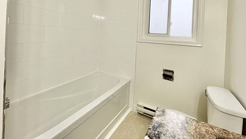 A white bathroom with a tub, toilet, and window.