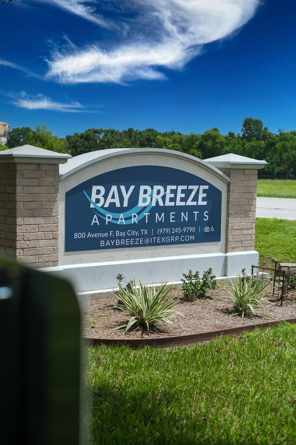 a sign for bay breeze apartments in front of a grass field