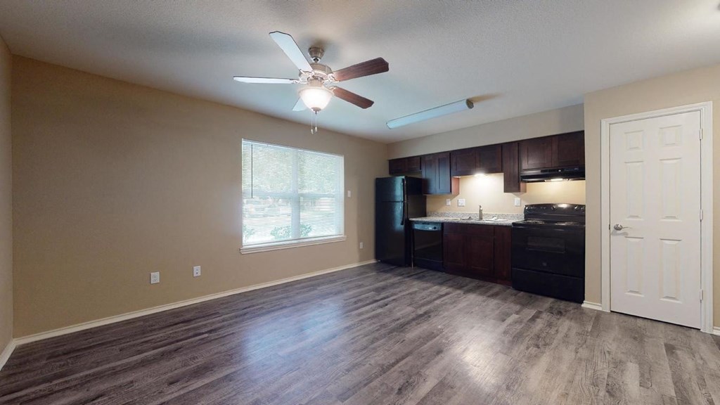 an empty living room with a ceiling fan and a kitchen