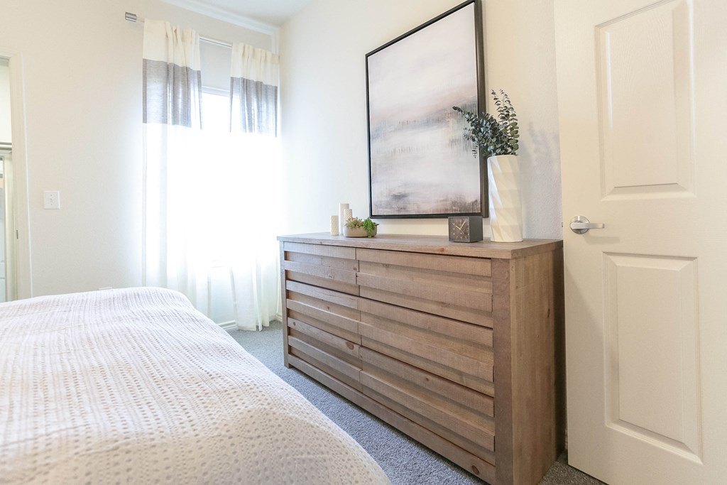 a bedroom with a dresser and window with white curtains