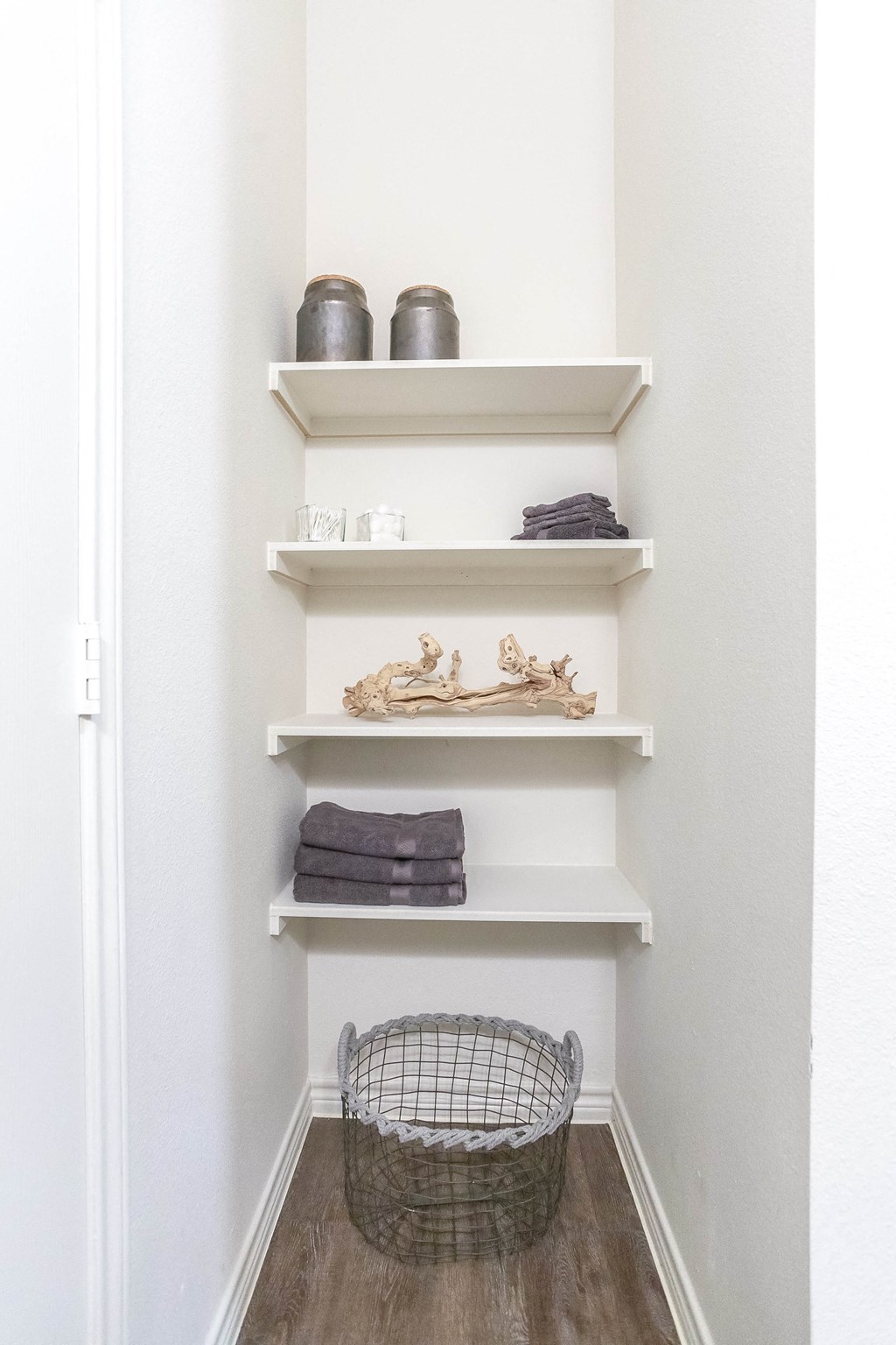 a small closet with white shelves and a basket on the floor