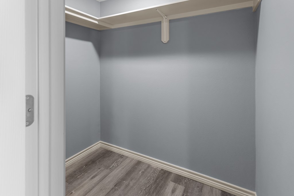 a walk in closet in a bedroom with grey walls and a wooden floor