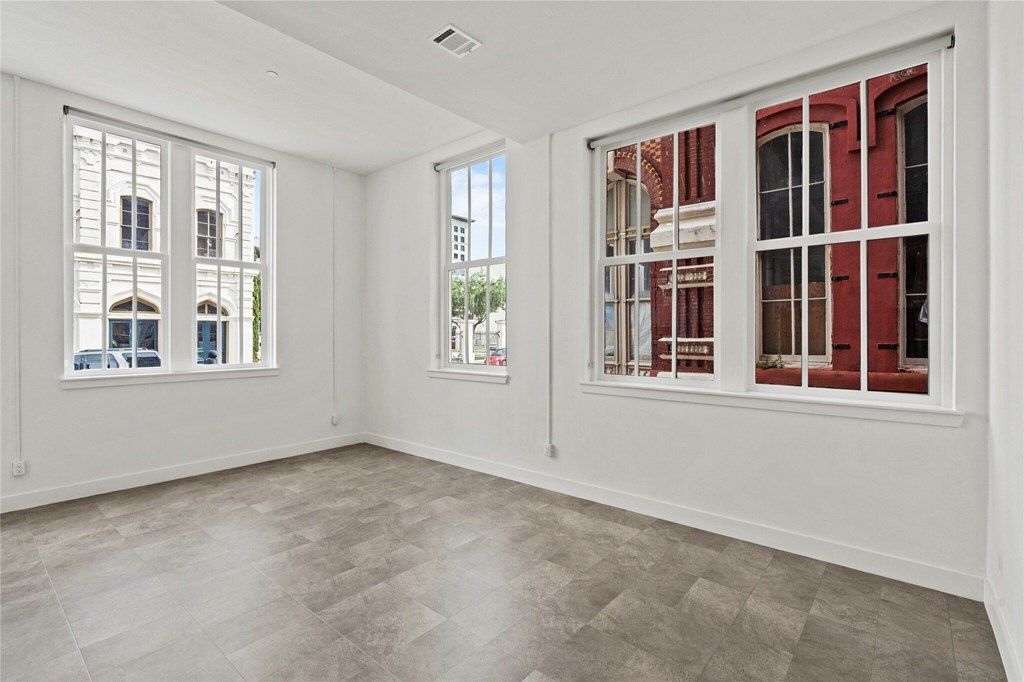 A room with white walls and a grey floor with two windows.
