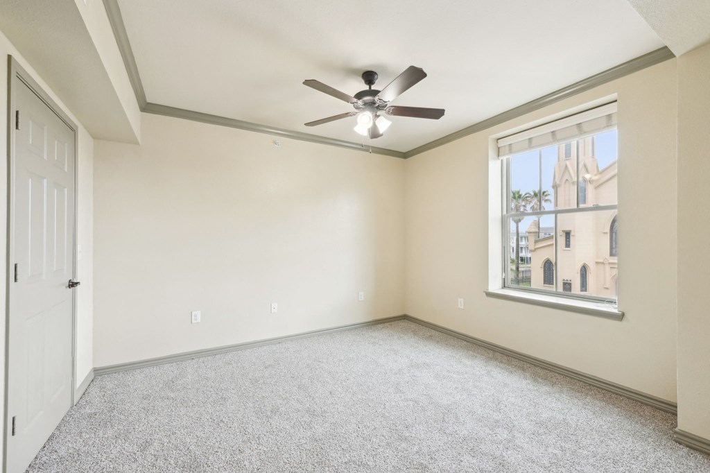 A room with a ceiling fan and a window overlooking a building.