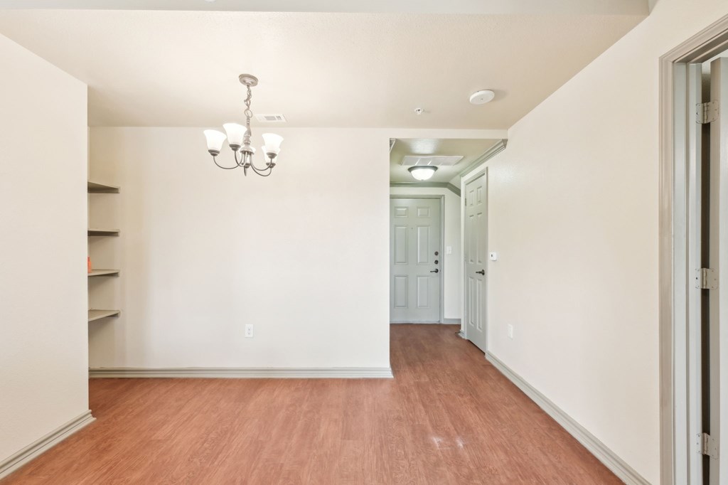 A long hallway with a chandelier and a door at the end.
