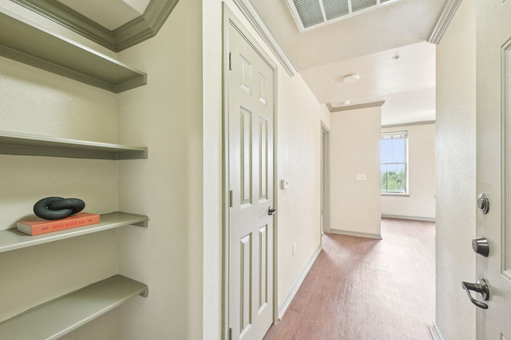 A hallway with a door on the right and a shelf with a book and a bowl on it.