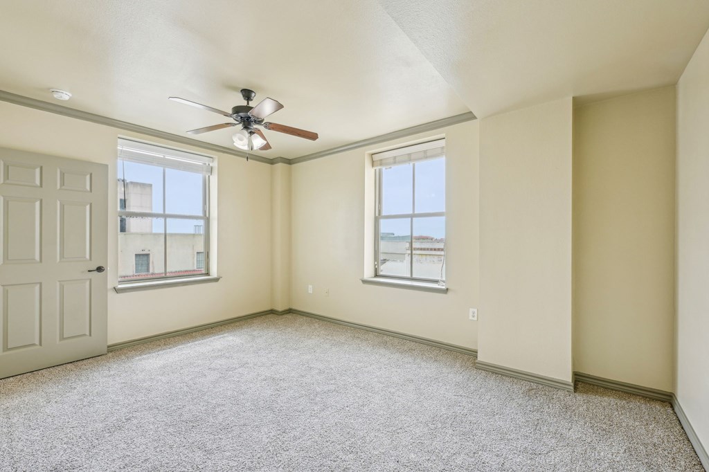 A room with a ceiling fan and two windows.