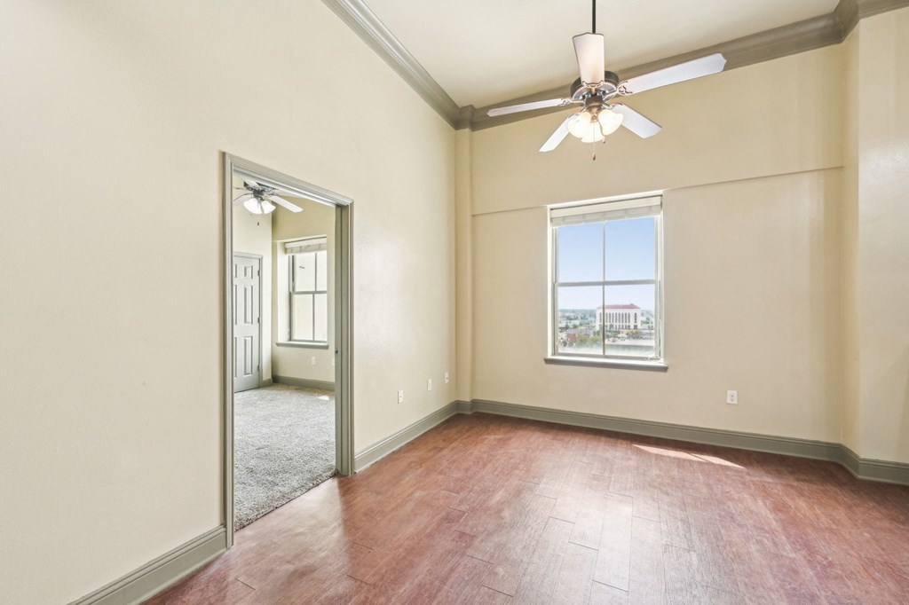A room with a ceiling fan and a window with a view of a city.