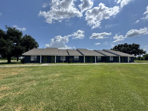 A large building with a grey roof is surrounded by a grassy field.