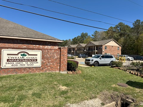 A sign for Twelve Oaks Apartments is in front of a brick building.