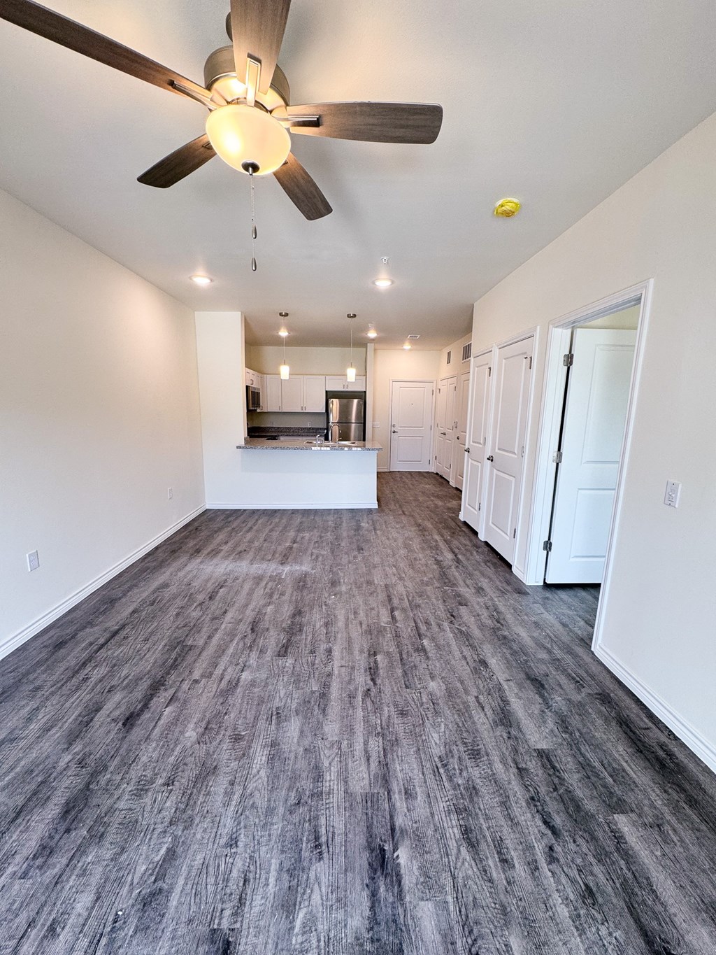 A room with a ceiling fan and a kitchen area in the background.