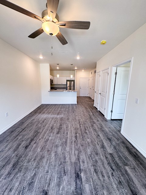 A room with a ceiling fan and a kitchen area in the background.