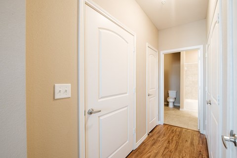 A hallway with a white door and a toilet visible in the distance.
