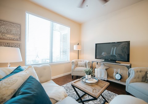 A living room with a white couch, a wooden coffee table, and a television on the wall.